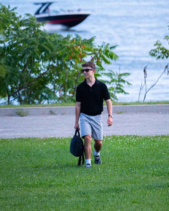 Walking along the water with a bag, wearing Relay glasses.